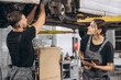 © anatoliycherkas - Young expert female inspects repair checklist with automotive mechanic worker partner, quality suspension technician team at fix garage. Vehicle maintenance service works industry occupation job.