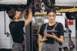 © anatoliycherkas - Young expert female inspects repair checklist with automotive mechanic worker partner, quality suspension technician team at fix garage. Vehicle maintenance service works industry occupation job.