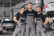 © anatoliycherkas - Group of three car service technician men and woman talking at workplace, people working together at vehicle repair garage service shop, check and repair customer car at automobile service center.