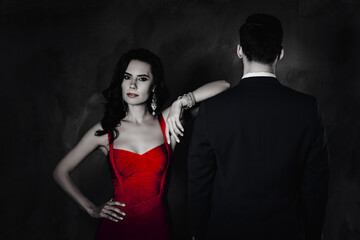 Poster - Portrait of charming lady with curly hair in purple dress with bijoutery looking at camera holding hand on waist lean on shoulder of man with rear back view isolated on grey background
