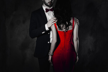 Poster - Cropped portrait rear view of pretty brunette woman with curly hair in violet apparel harsh half face man in tuxedo bowtie holding hands shoulders lover mysterious couple isolated on grey background