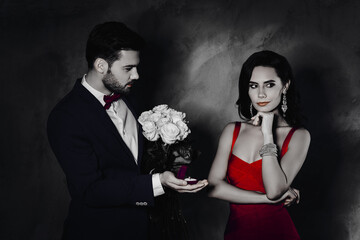Poster - Will you marry me Portrait of gentleman with bristle giving gold ring with diamond to minded ponder lady with jewelry holding white roses, hand on chin, couple isolated on grey background