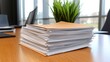 © Manon - A stack of organized paperwork rests on a wooden table, accompanied by a small green plant, suggesting a workspace or office environment.