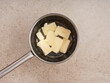 © Food Images - A saucepan holds several cubes of butter as they slowly melt on the stovetop. The kitchen countertop is light-colored, indicating a tidy cooking area