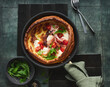 © Food Images - A delectable Yorkshire pudding is filled with slices of prosciutto, creamy mozzarella, and vibrant cherry tomatoes, garnished with fresh greens, placed on a dark textured surface