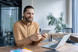 © Liubomir - Smiling professional in casual attire working with a tablet in a modern office environment. A laptop is placed on the desk next to him, depicting a productive and professional setting.