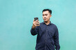 © Khoirul - Asian man standing holding smartphone making video call, isolated green background