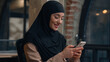 © Yuliia - Muslim woman in hijab islamic girl Arabian businesswoman entrepreneur calm smiling business lady working at desk scrolling mobile phone gadget addicted female online app cellphone internet in office