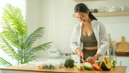 Wall Mural - Young woman in sportswear preparing variety of fresh vegetables in storage containers for healthy meal storage. Healthy lifestyle and nutrition concept.