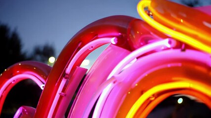 Aufkleber - Vivid pink and orange neon tubes casting intricate glowing patterns against darkening urban sky, highlighting luminescent architectural details with electric energy