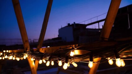 Aufkleber - Warm light bulbs glowing softly over wooden construction beams, illuminating industrial site during blue hour with soft, cozy ambiance against darkening sky