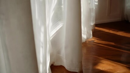 Aufkleber - Sunlight streams through an open window, illuminating white curtains gently swaying in the breeze and casting dancing shadows on a polished wooden floor in a serene, bright room