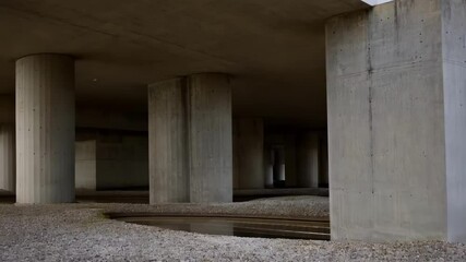 Aufkleber - Concrete pillars support an elevated building, showcasing modern architectural design and construction techniques with gravel landscaping and a subtle water feature