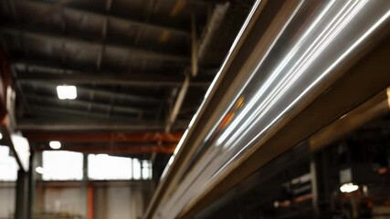 Fototapete - Light reflections glide over a polished steel beam in a large industrial factory, highlighting the beam's smooth surface and the surrounding industrial environment