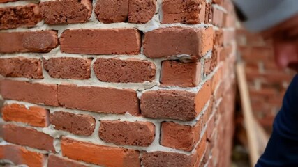 Poster - Construction worker wearing white hard hat carefully laying red bricks, spreading mortar and creating sturdy wall structure with professional masonry technique