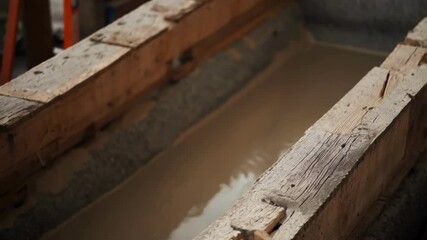 Aufkleber - Liquid concrete streaming into wooden formwork, forming foundational base for emerging architectural structure at active construction site with ongoing development work