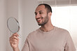 © New Africa - Smiling man looking at mirror in room