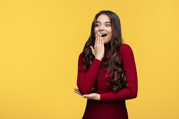 Wall Mural - Shocked young woman in red dress is posing on yellow background.