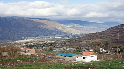 Wall Mural - Breathtaking Rural Landscape with Homes and Majestic Mountains Under a Cloudy Sky