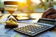 © Yuliia - Close-up of a hourglass with a businessperson's hand using a calculator to calculate an invoice - showing the pressure and time constraints in the world of finance.