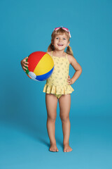 Wall Mural - Cute little girl in swimsuit with inflatable ball and swim goggles on light blue background