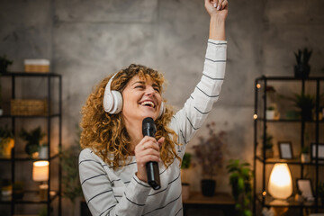 Wall Mural - happy adult woman listen music on headphones and sing on microphone