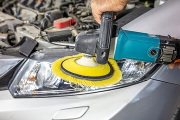 Car headlights cleaning with power buffer machine at car service. Big headlight cleaning with power buffer machine at service station. Car detailing concept. Auto cleaning and polish.