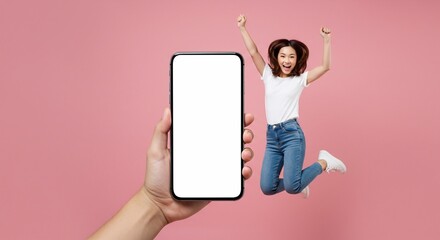 Full length of cheerful Asian woman jumping and smiling in air with showing cellphone blank screen with empty space for mobile app on screen. Isolated in studio pink background. Creative collage.
