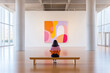 © OlgaKhorkova - Woman viewing colorful abstract art in modern gallery with large windows and wooden bench.