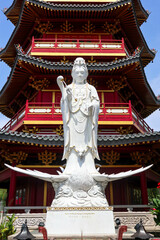 Wall Mural - A detailed close-up of a magnificent white Guan Yin statue, positioned in front of a vibrant red and gold Chinese pagoda.