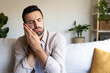 © Daniel - Caucasian man in pain suffering from toothache sitting on sofa at home. Copy space.