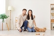 © Studio Romantic - Indoor shot of happy young married couple with small pet dog. Smiling young man and woman sitting on floor at home together with cute little fluffy brown bichon poodle. People, animals, family concept