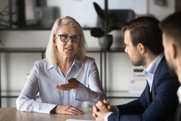 Wall Mural - Middle-aged businesswoman hold formal meeting with shareholders, business partners talking, met in boardroom, discussing potential cooperation, joint project details, brainstorm at briefing in office