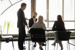 © fizkes - Team leader dressed in suit stand in front of meeting participants addressing, make speech, provide explanations about project or agreement details, share solutions, strategizing together in boardroom