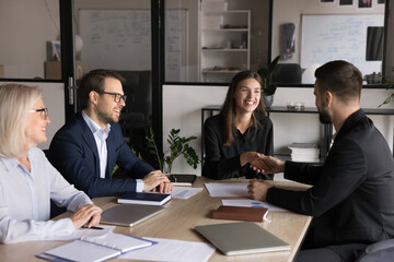 two business partners shaking hands in conference room at table during group meeting with project co