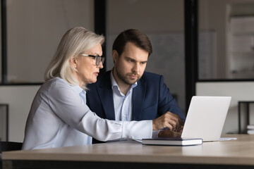 two 35s and 55s teammates sitting at desk, looking at computer monitor, working on common task, coll