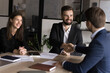 © fizkes - Two businessmen shaking hands across table, gesture of trust, agreement, closing of deal. Business parts gather in conference room, start or finalize negotiation feel satisfied, express mutual respect