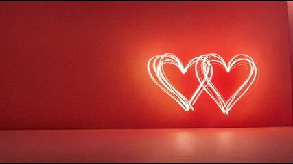 Poster - Light painting of two hearts intertwined symbolizing love and connection, set against a vibrant red backdrop, perfect for valentine's day or romantic themes