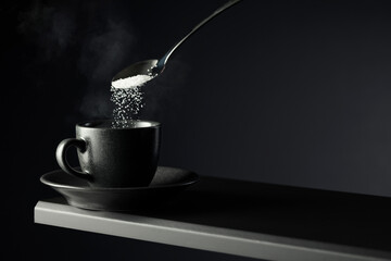 Wall Mural - Sugar is poured into a black cup of coffee on a black background.