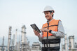 © PhugunStock - Smiling Asian male engineer wearing safety uniform standing in front of oil refinery with tablet device To inspect the operation of the oil refinery Petrochemical Gas Industry Engineer