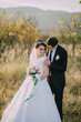 © Vasil - A bride and groom are standing in a field, with the bride holding a bouquet and the groom wearing a tie. Scene is romantic and happy, as the couple is posing for a picture together