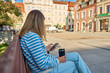 © Lazy_Bear - Woman is using smartphone and holding reusable coffee cup while sitting on bench in city park