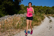© Lazy_Bear - Woman running on rocky trail surrounded by lush greenery and trees under clear blue sky. Fitness workout outdoors. Female trail runner have cardio training on sunny day