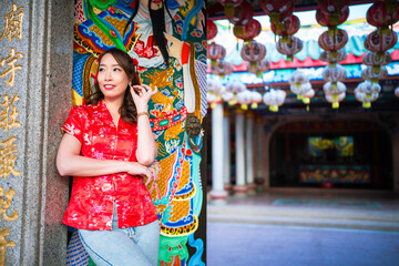 A woman in a red Chinese dress stands in front of a building with a large painting of a woman on the wall