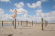 © Milou Dirks - elegant woman on the beach in long white dress standing on poles on windy day in artistic portrait