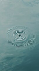 Poster - Single water droplet falling onto a calm turquoise water surface, creating expanding concentric ripples, offers a tranquil and mesmerizing view