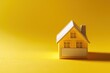 © Nopadon - A small yellow paper house on a bright yellow background, symbolizing home, warmth, and creativity.