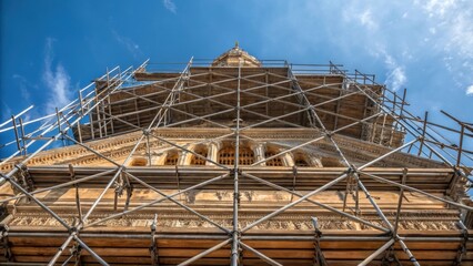 Aufkleber - A medium closeup of intricate scaffolding crisscrossing against the backdrop of a blue sky emphasizing the geometric patterns and structural elegance that support the building