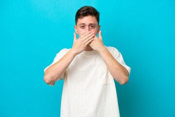 Wall Mural - Young handsome Brazilian man isolated on blue background covering mouth with hands