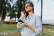 © SHOTPRIME STUDIO - Sunglasseswearing woman checks her phone while standing in a park, surrounded by palm trees